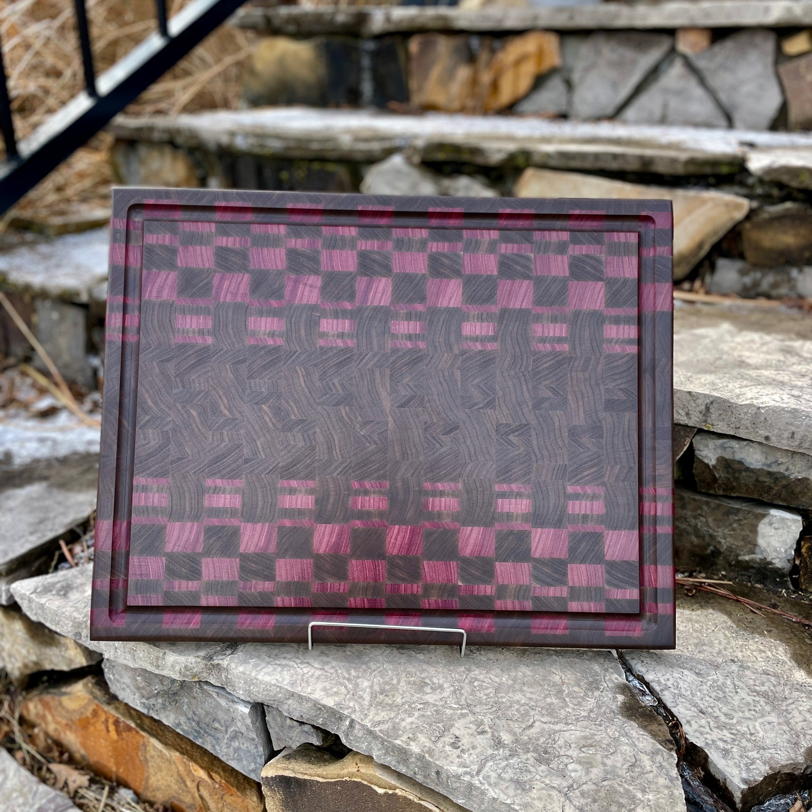Walnut and Purpleheart Amethyst Mosaic End Grain Cutting Board with juice groove and a stone background.