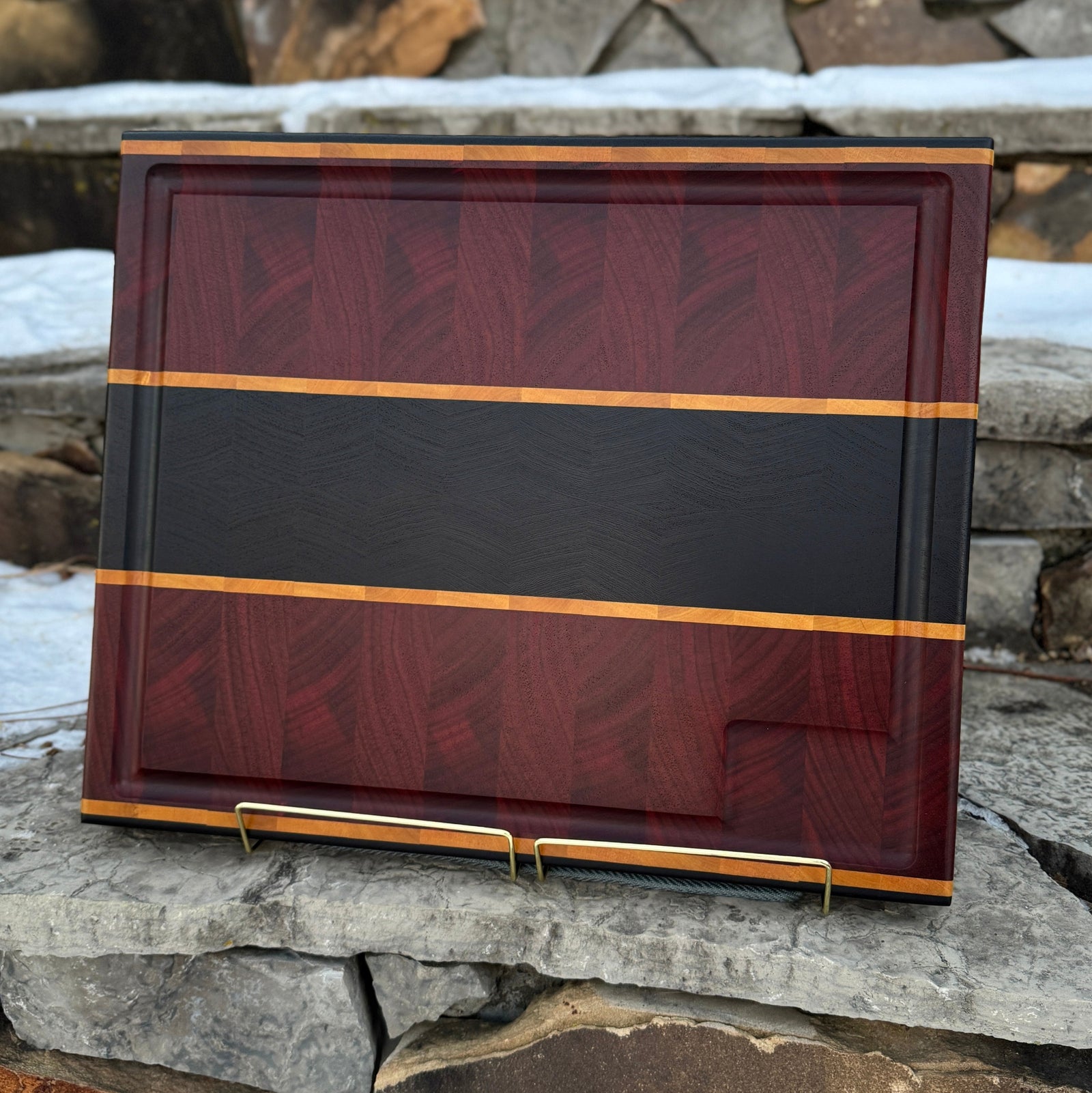 A padauk and wenge end grain cutting board with yellow heart inlays on a stone background 
