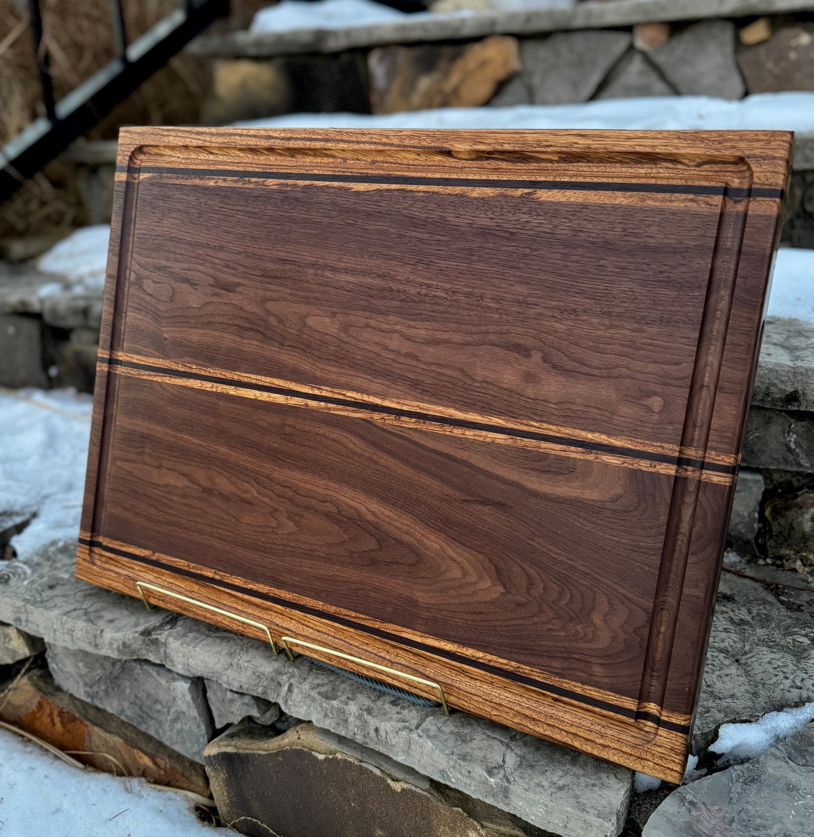 A walnut, zebrawood and wenge edge grain cutting board with a stone background