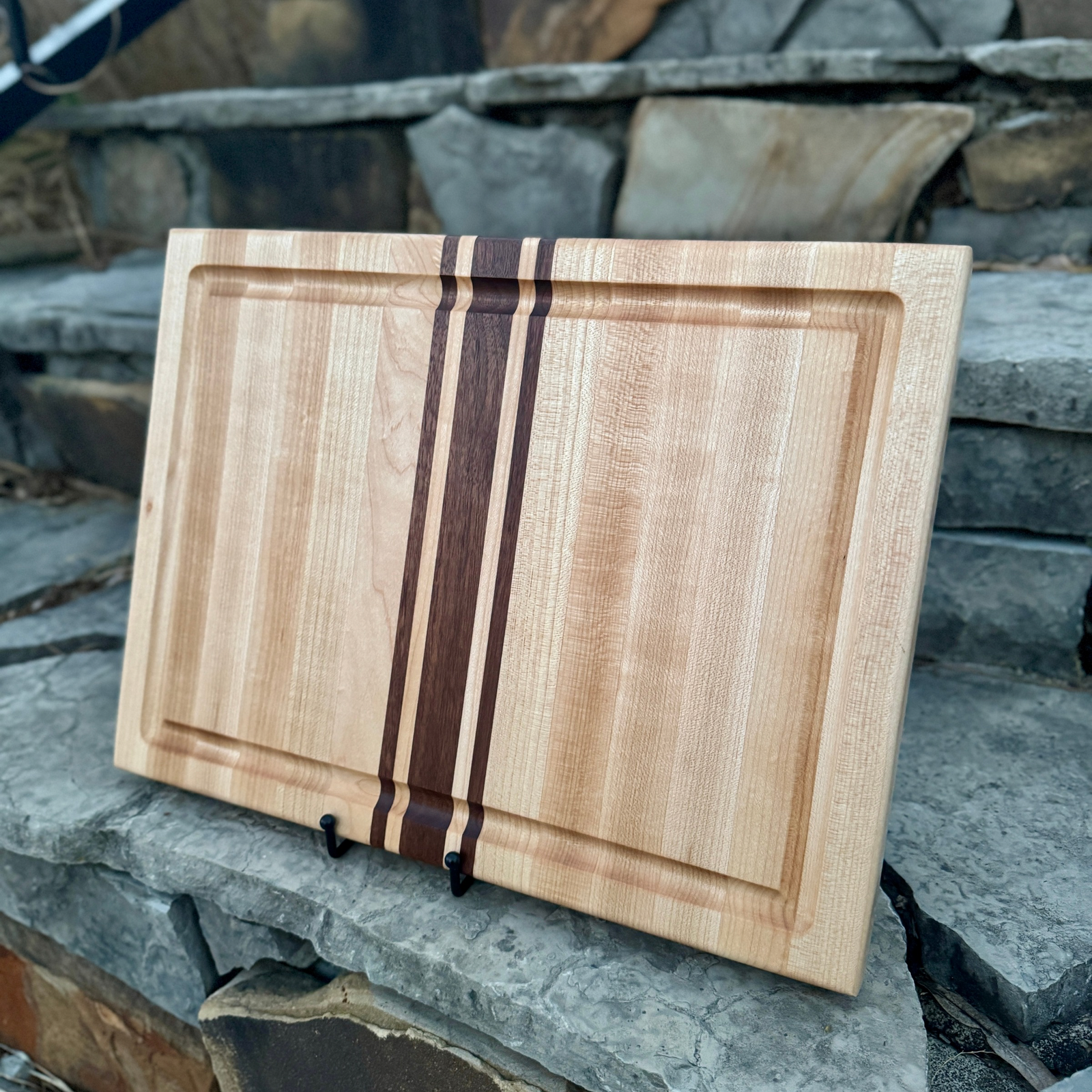 Maple and Walnut Cutting board with a juice groove and a stone background.
