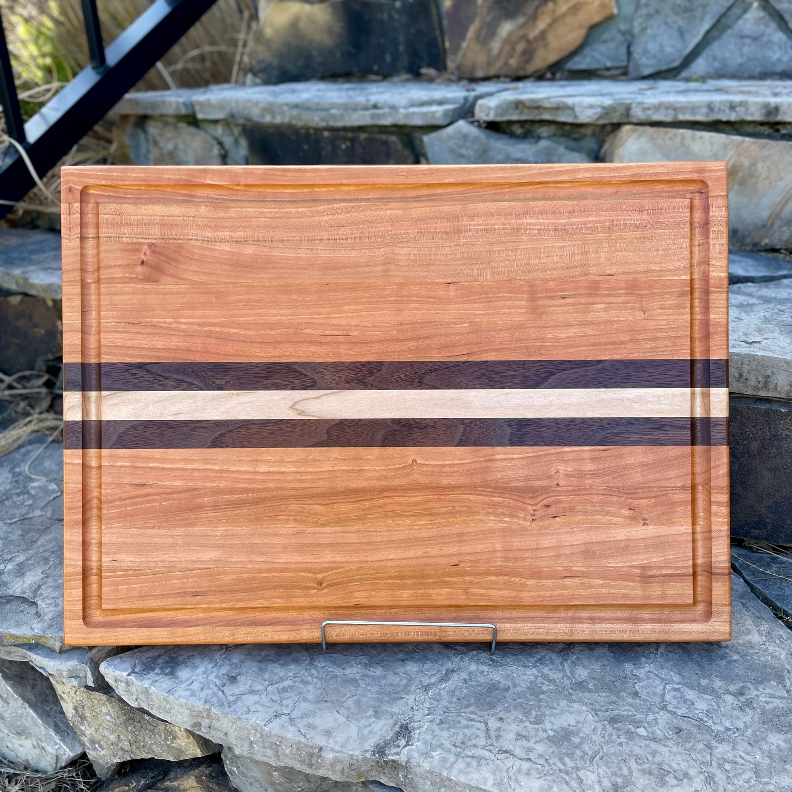 A beautiful cherry cutting board with maple and walnut inlays running down the middle of the board.