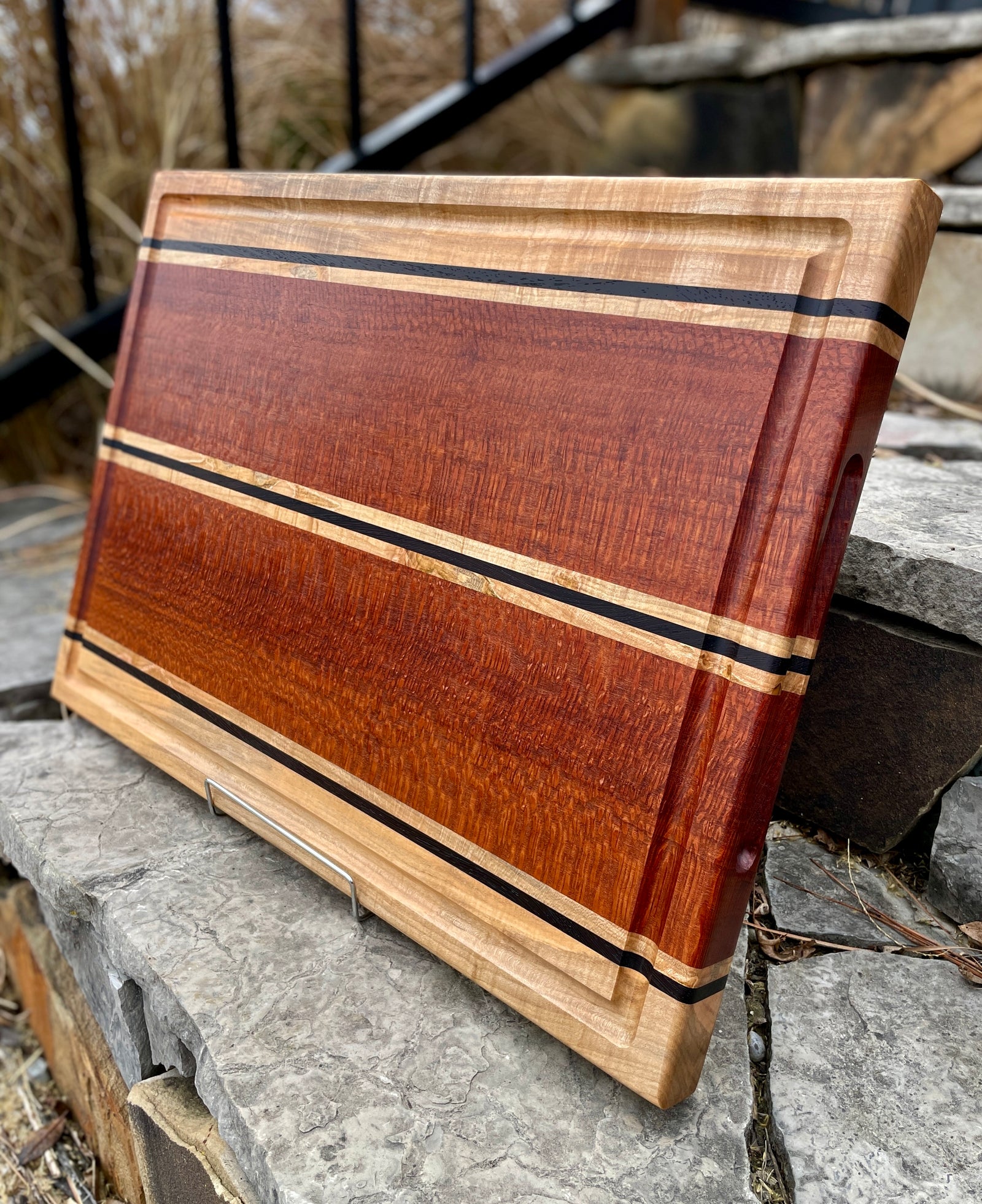 A leopard wood, wenge and figured maple edge grain cutting board with stone background