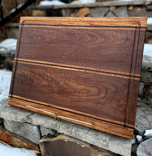 A walnut, zebrawood and wenge edge grain cutting board with a stone background