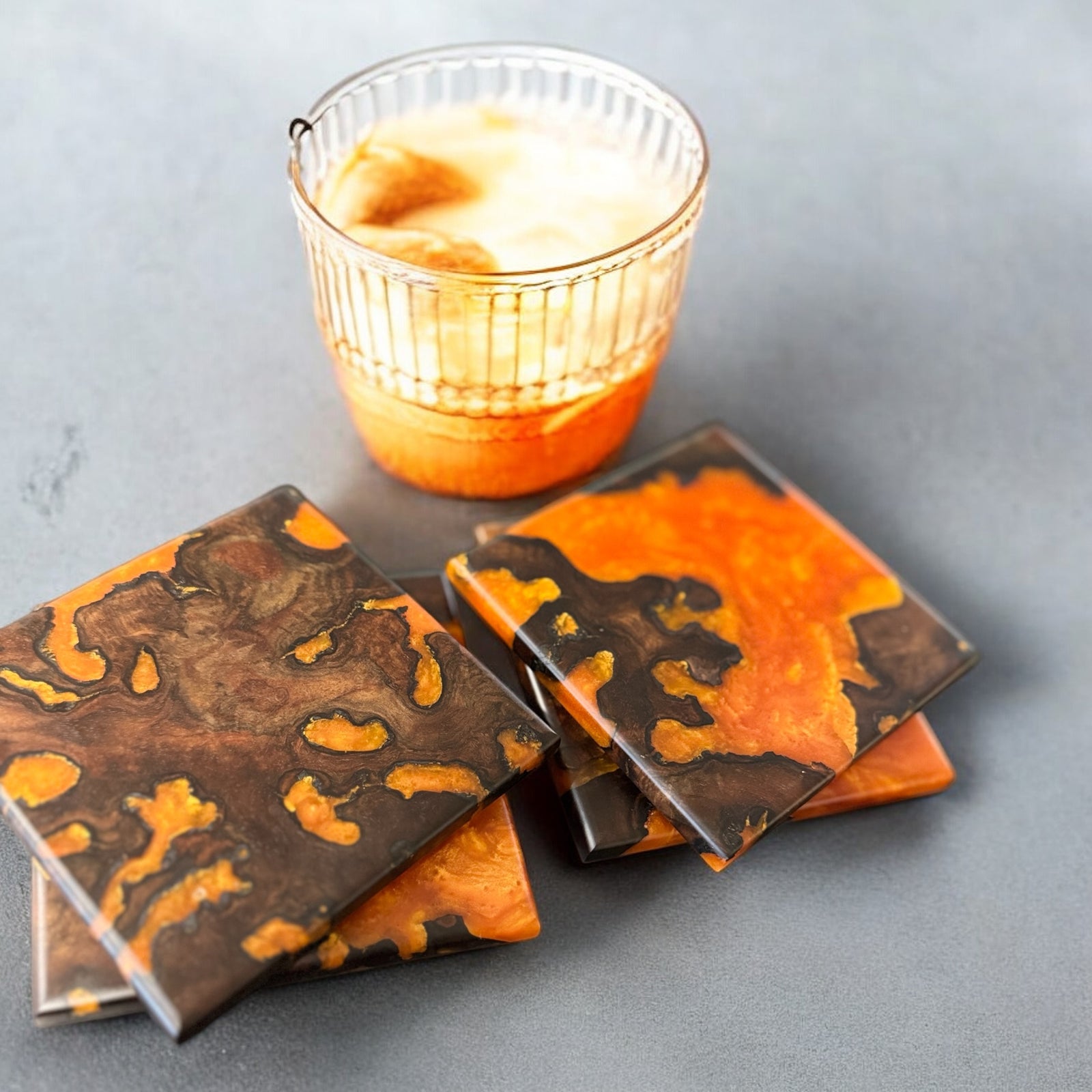 Walnut Burl coasters with Orange Resin on a gray concrete top with a special orange drink.
