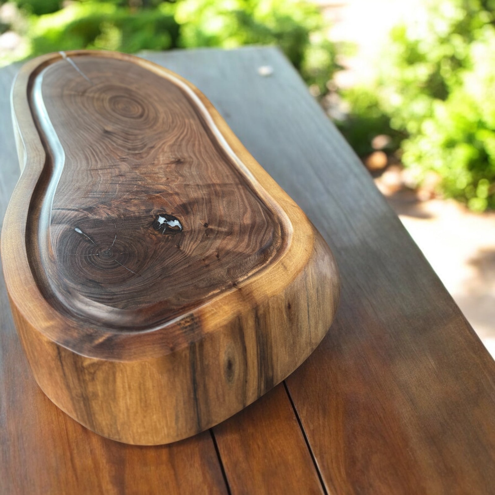 Live Edge Walnut Cutting Board with a juice groove sitting on an outdoor wood table.